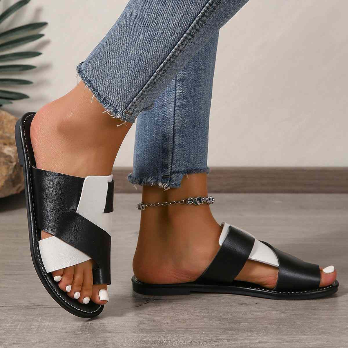 Toe post flats sandals with black and white straps, worn by a person in jeans.