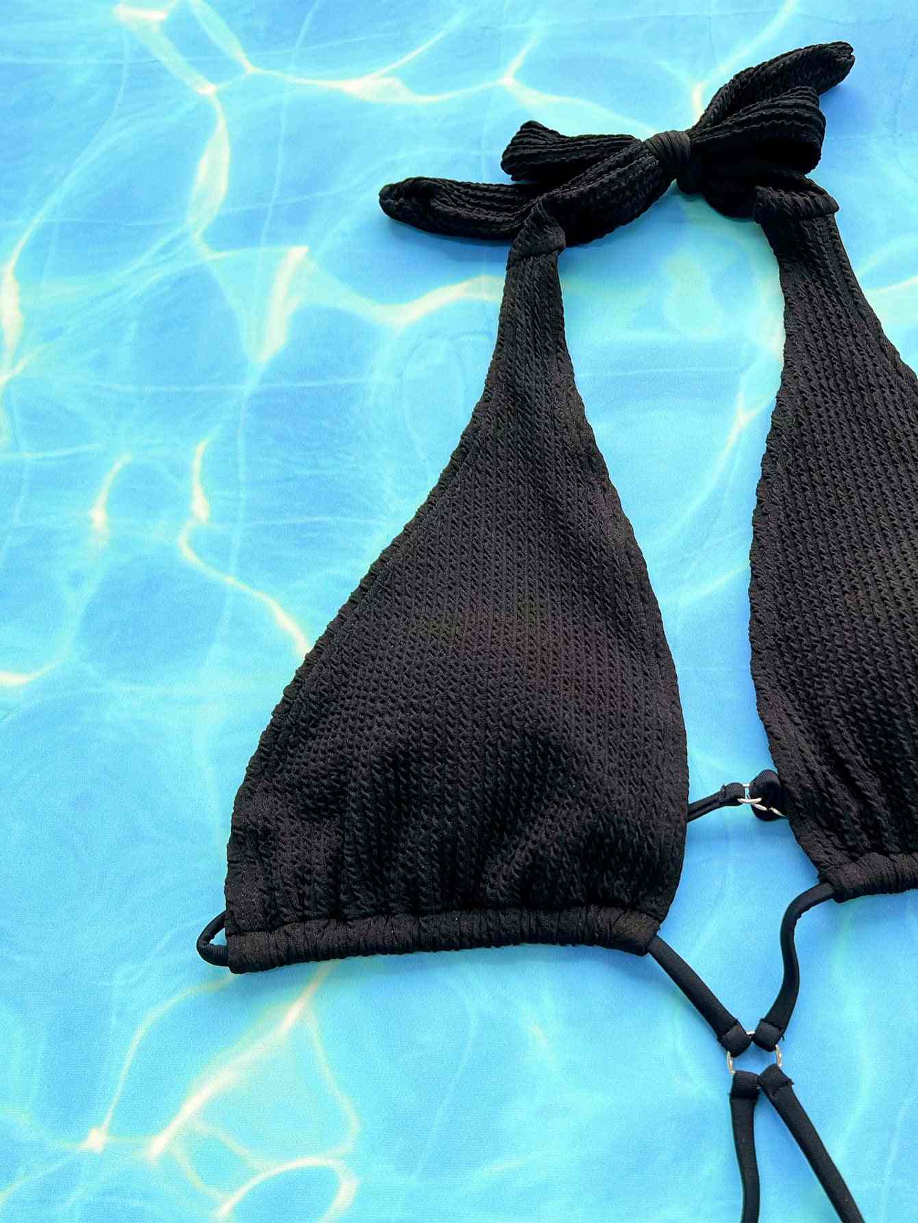 Halter neck side tie one-piece swimsuit in black against a water background.