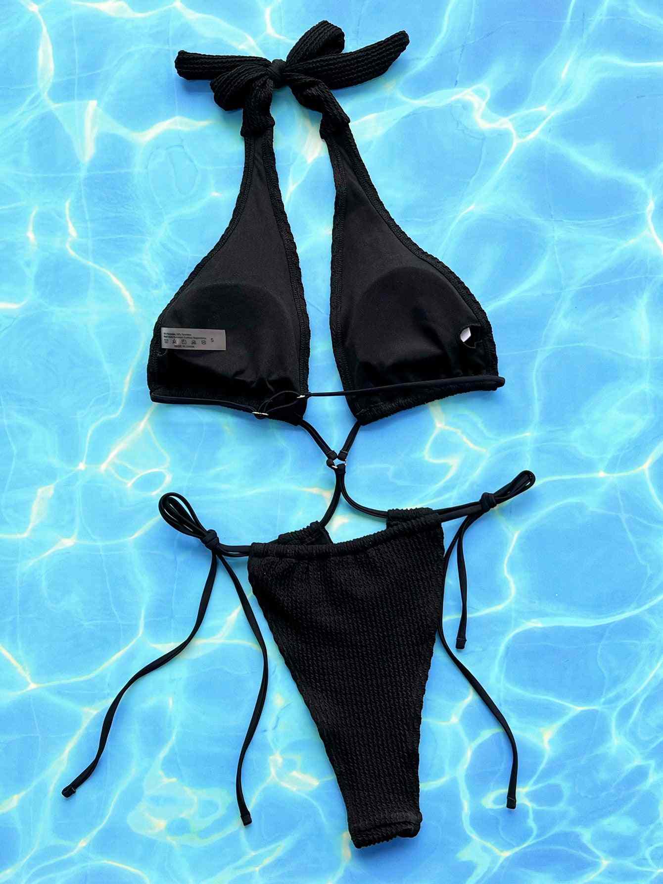 Halter neck side tie one-piece swimsuit in solid black on a blue background.