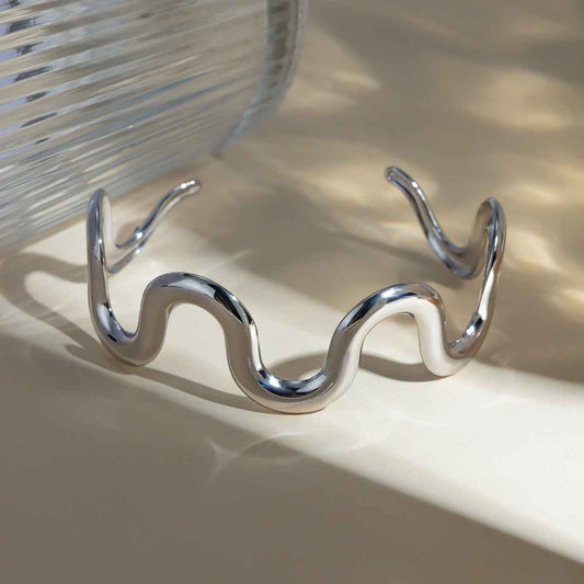 Stainless steel wave shape bracelet on a light surface.
