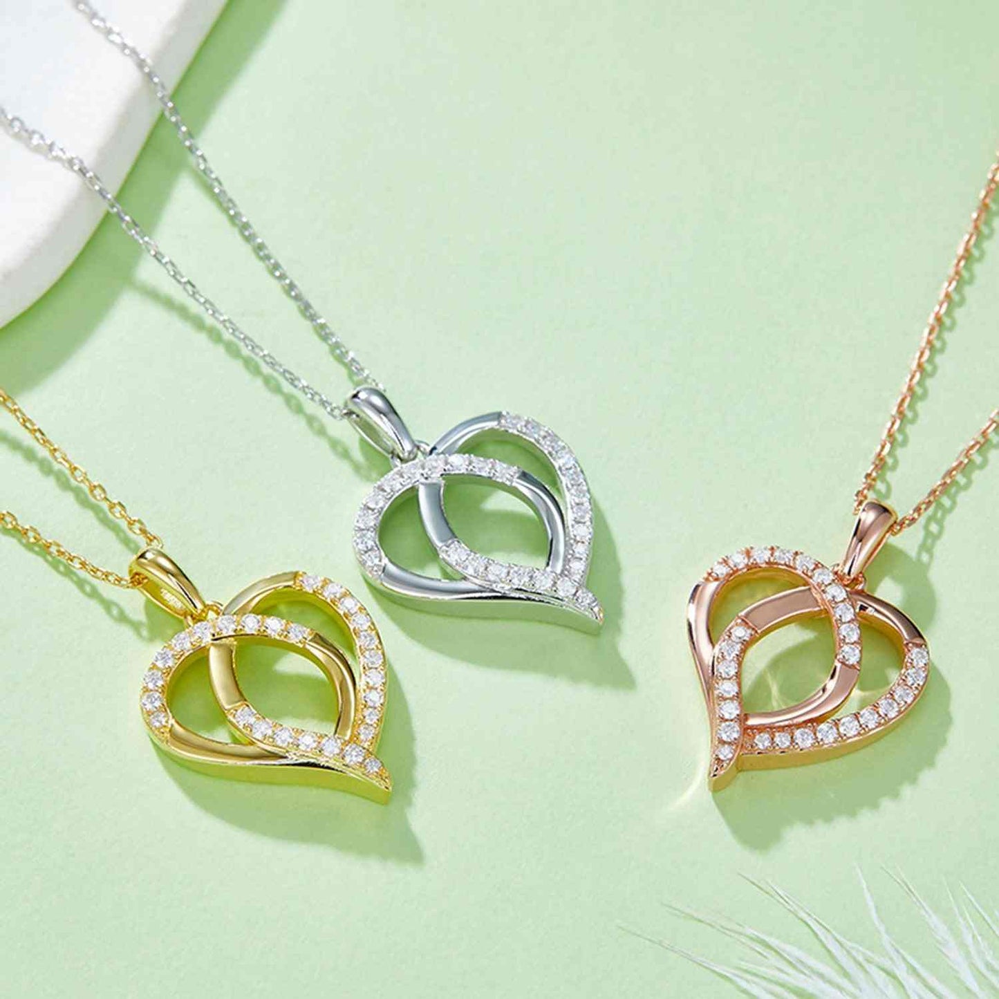Moissanite 925 sterling silver heart shape necklace in gold, silver, and rose gold-plated designs on a green background.