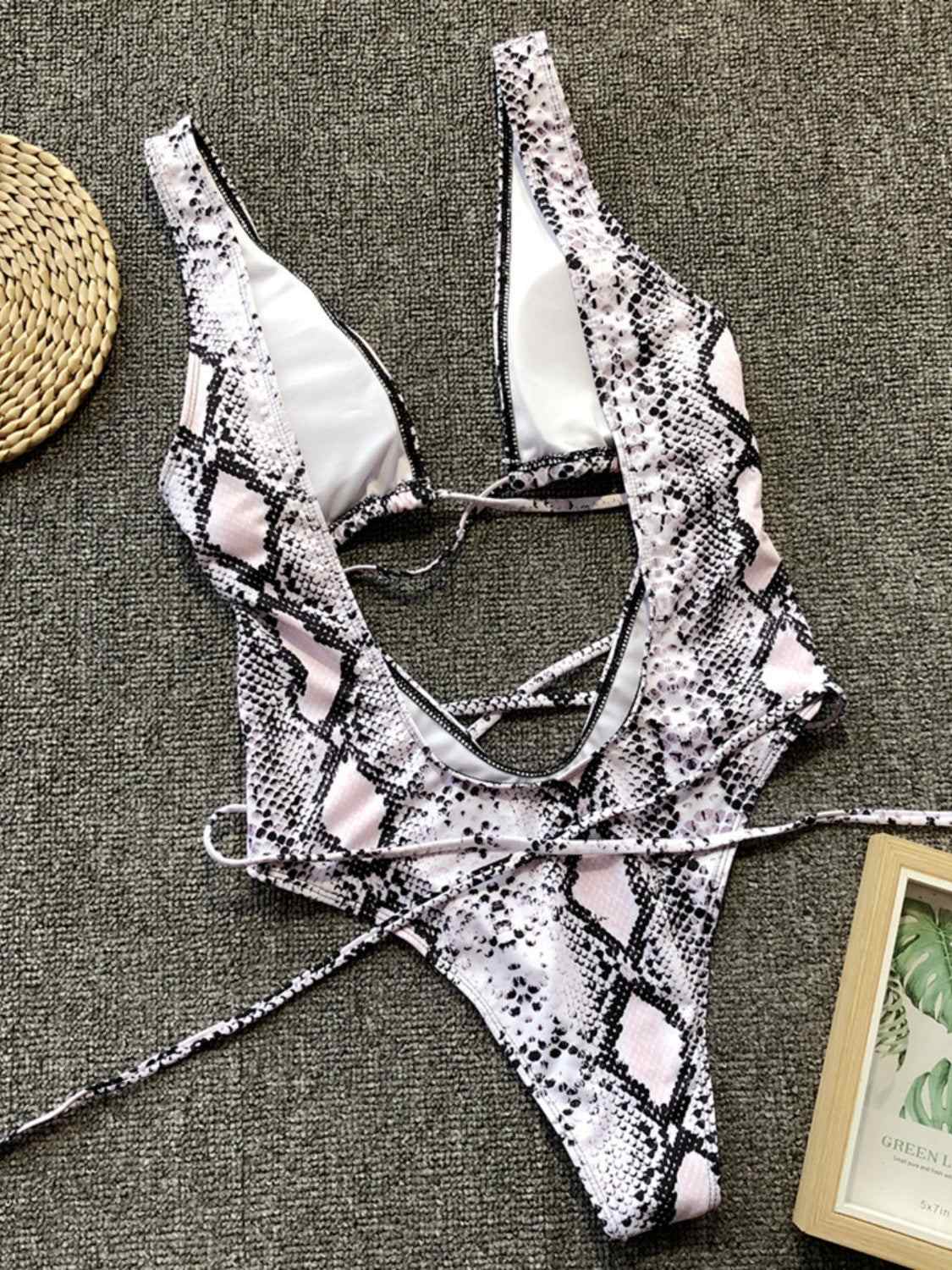 Lace-up backless plunge one-piece swimwear with snake print design laid flat on fabric.