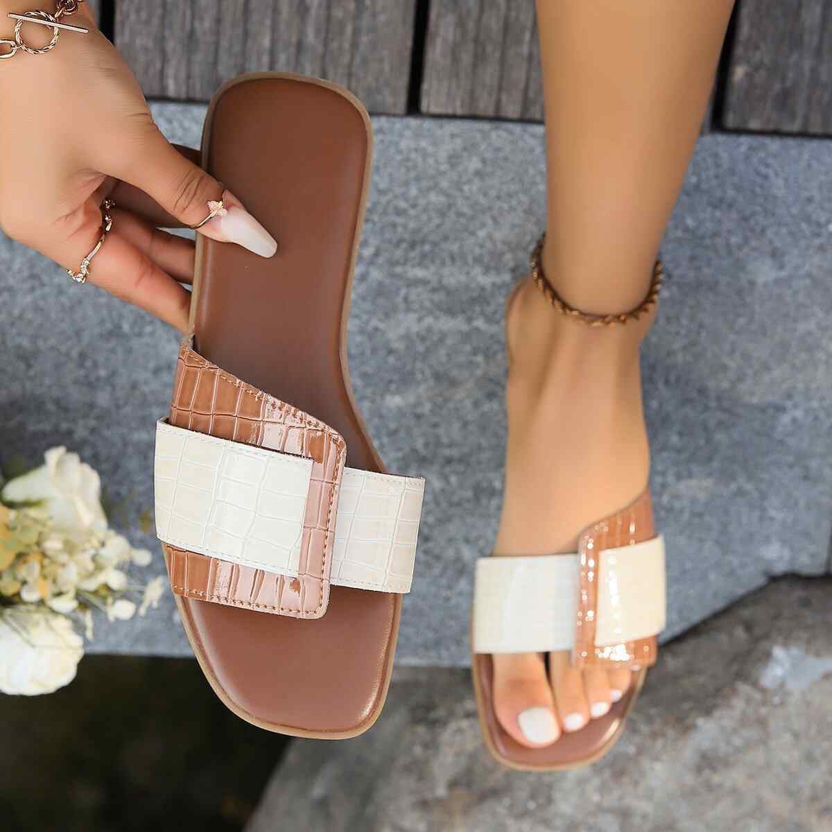 Open toe flats sandals in PU leather with textured straps on a wooden surface.